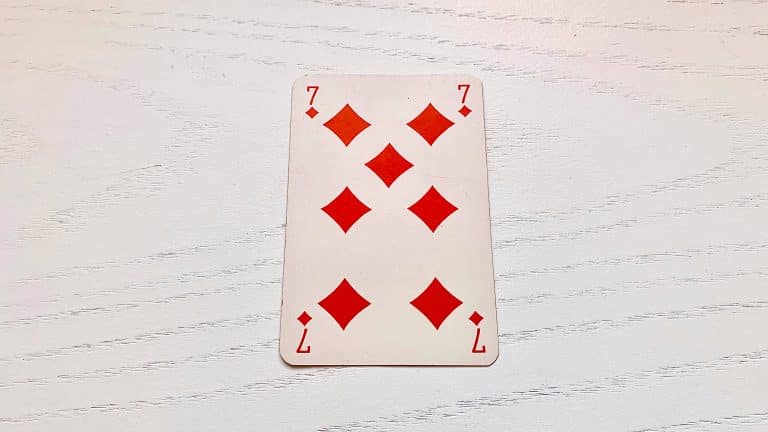 Carte du 7 de Carreau disposée face visible sur un support en bois sombre.