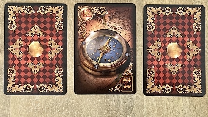 Carte La Boussole 42 Gilded Lenormand flanquée de deux cartes face contre table lors d'un exercice d'association.