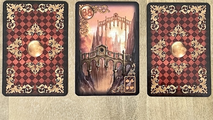 Carte Les Ponts 38 Gilded Lenormand entourée de deux cartes retournées sur un fond de bois clair.