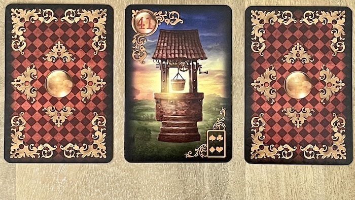 Carte Le Puits 41 Gilded Lenormand disposée entre deux cartes cachées pour symboliser les interactions.