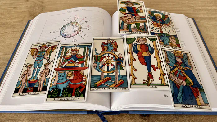 Arcanes du Tarot de Marseille posés sur un livre d'astrologie ouvert à la page d'un thème astral