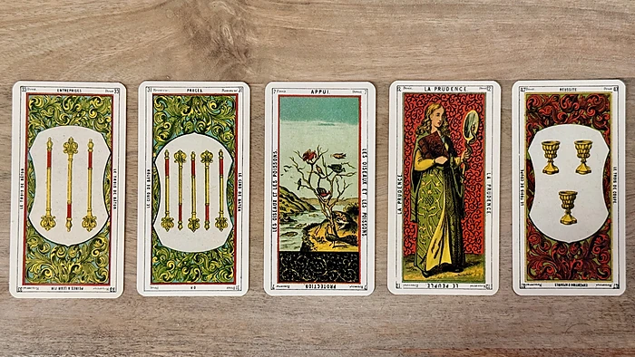 Tirage 5 cartes du tarot égyptien Oracle des Dames : Entreprises, Procès renversé, Appui, La Prudence et Réussite posées en ligne sur une table en bois