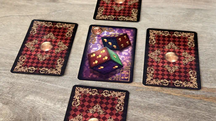 Focus sur la carte Les Dés 39 du Gilded Lenormand au milieu d'une croix de cartes aux dos rouge et or.