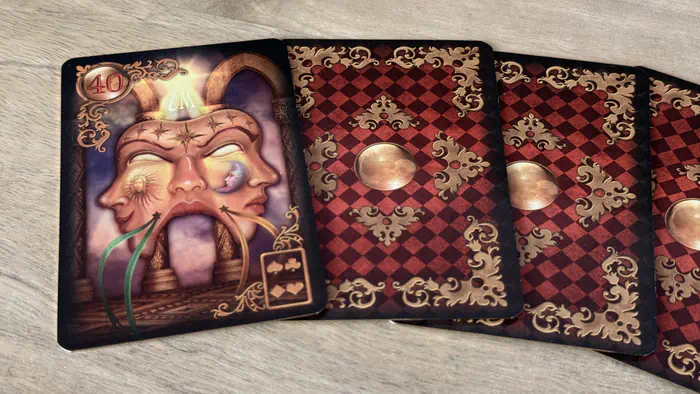 Carte Le Masque 40 Gilded Lenormand évoquant les apparences et les secrets posée à gauche d'un éventail de cartes.